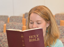 Young blond woman smiling while reading in the bible sitting in church. 
