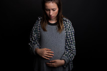 A pregnant teenager looks at her stomach with a solemn look.