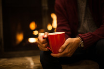 sitting in front of a fireplace holding a mug 