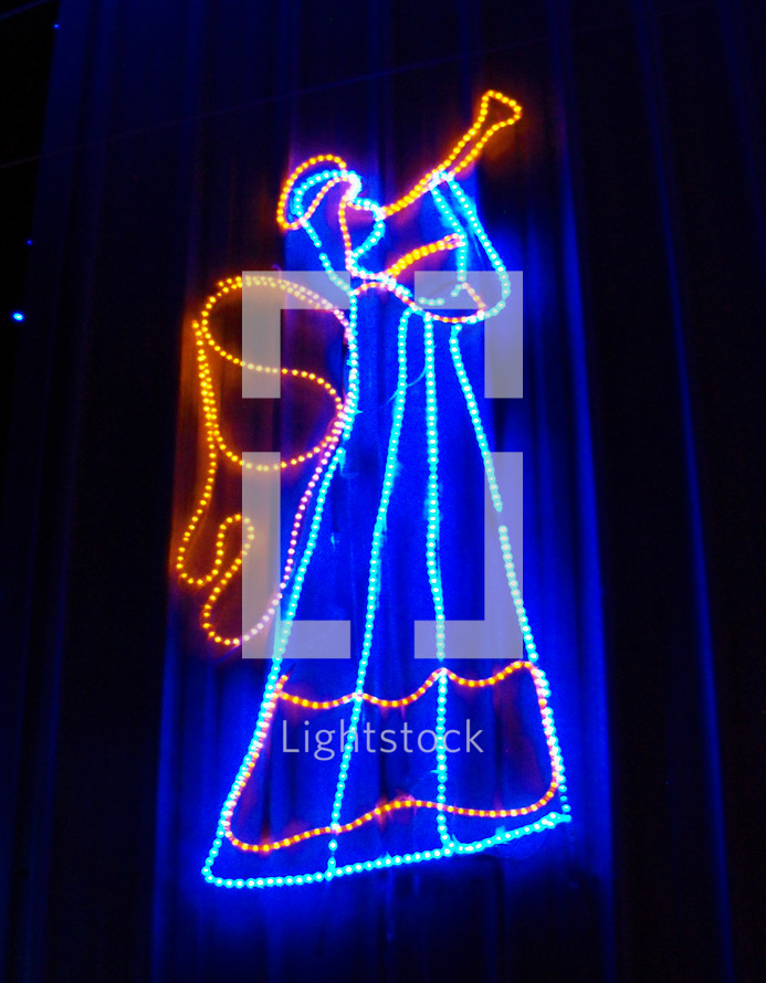 angel trumpeter Christmas light display in blue and gold colors against the night sky like a holographic image lighting up the night sky during Christmas time to announce the coming of Jesus Christ. 