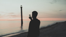 a man taking a picture of water lapping onto a shore at sunset 