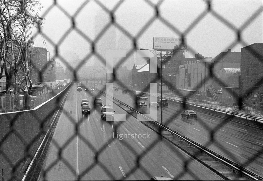 A busy highway seen through a chain link fence.