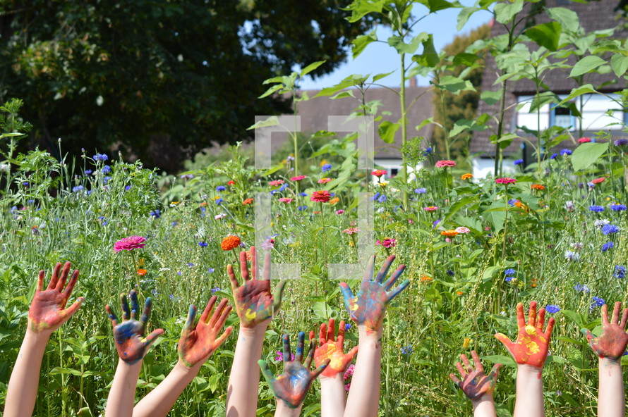 finger paint on the hands of kids standing outdoors in a field of flowers 