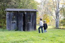 Boys walking through a field towards a rustic shack.