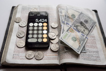 money, and calculator app, on an opened Bible 