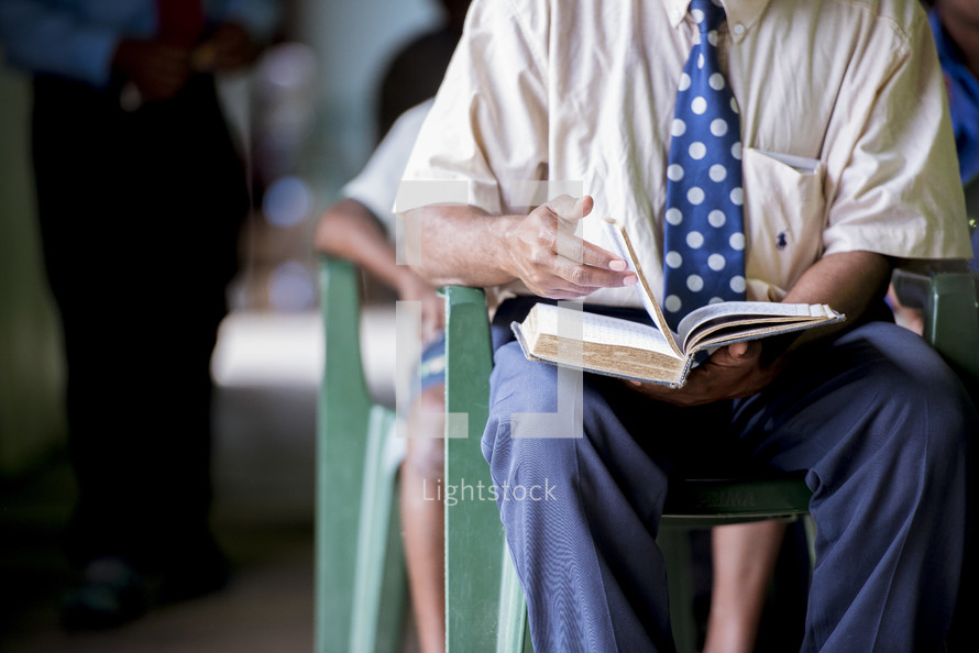 a man sitting reading a Bible during a worship service 