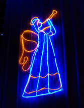 angel trumpeter Christmas light display in blue and gold colors against the night sky like a holographic image lighting up the night sky during Christmas time to announce the coming of Jesus Christ. 
