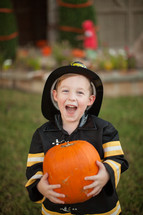 boy in a firefighter costume holding a pumpkin 