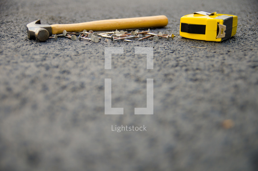 hammer, nails, and tape measure on asphalt 