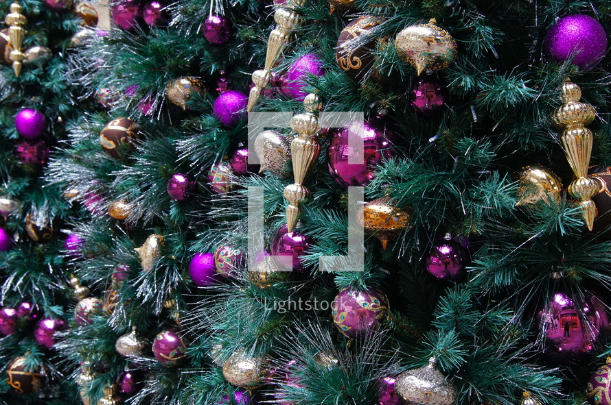 Purple and gold ball Christmas ornaments hanging from pine Christmas tree.
