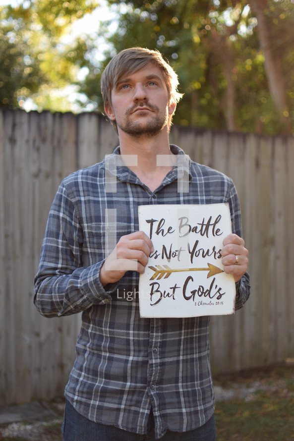 A man holding a sign The Battle is not yours, But God's, 1 Chronicles 20:15
