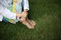 A woman in sandals sits in green grass.