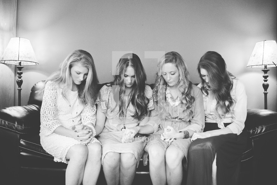 women's group holding hands in prayer on a couch 