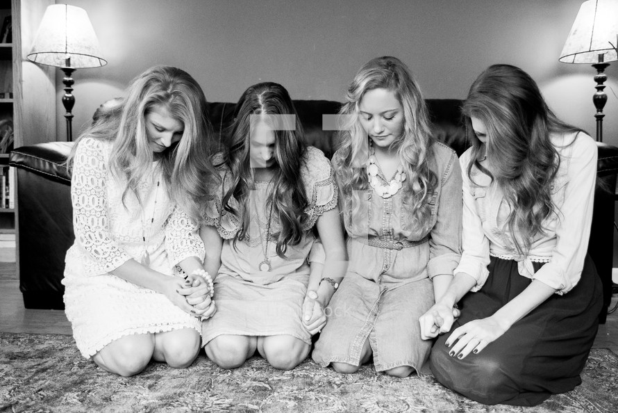 women's group holding hands in prayer on the floor in front of a couch 
