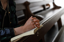 a woman sitting in a pew with praying hands holding a rosary 