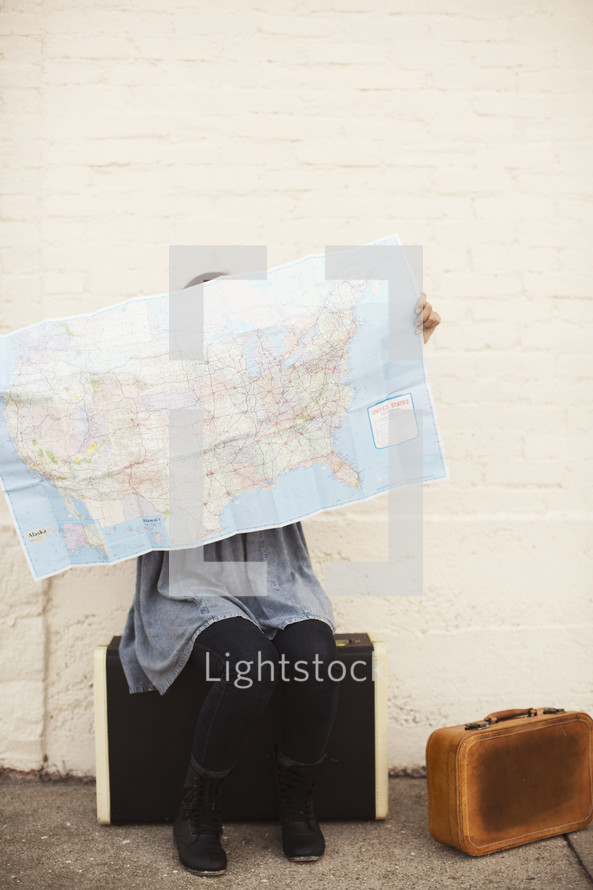woman sitting on suitcases looking at a map 
