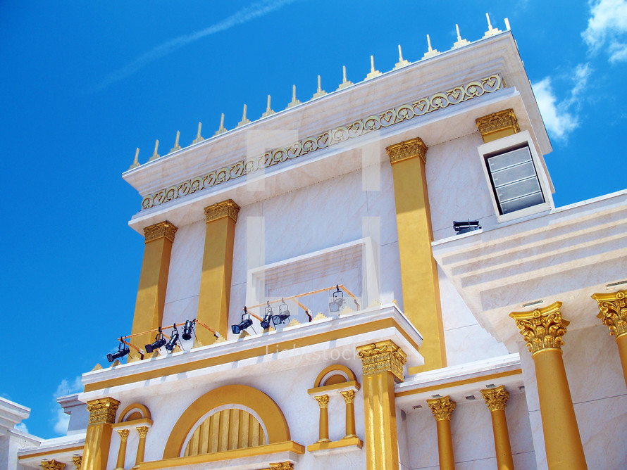 A replica of an Ancient Jewish Temple  with gold pillars, doors and columns against a stone white and marble building  against a light blue sky just like the Jewish temples of old during ancient bible times. 