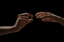 Photograph of a man and woman exchanging vows and wedding rings. Studio portrait with black background.