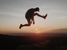 Silhouette of man leaping over a canyon at sunset.