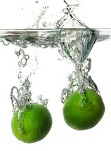 Limes submerged into water creating a splash.