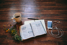open Bible, journal, pen, earbuds, iPhone, and flowers on a table 