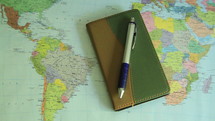 Close-up of a notebook with a pen and world map on the desk.