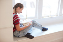 girl reading a book in a window seat 