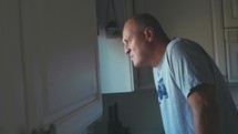 a man looking out a window in his kitchen 