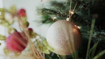 A golden ball ornament on a decorated Christmas tree with branches and lights.