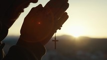 Man prays at sunset with rosary