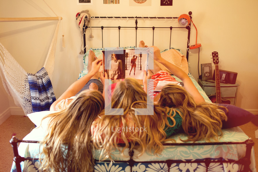 three sisters lying on a bed looking at a magazine 