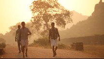 men walking down a dirt road through a village 