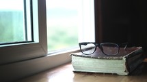 reading glasses on a Bible in a window 
