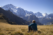 Man in a grassy field in front of mountains with snow