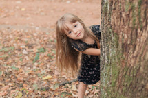 a girl peeking around a tree 