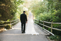 bride and groom holding hands walking across a wood bridge
