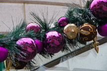 Purple and gold ball Christmas ornaments with pine needle branch along stair rail.