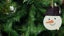 Snowman decoration on a Christmas tree with snow falling 