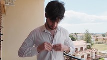 Young Boy Buttons His White Shirt On The Balcony At Home