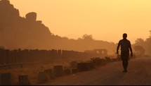man walking down a dirt road at sunset 