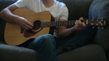 a young man sitting on a couch playing a guitar 