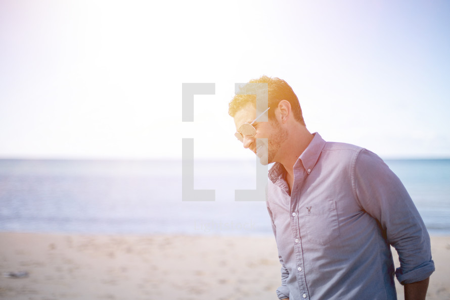 man in sunglasses standing on a beach 