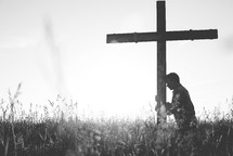 a man standing in a field next to a cross praying 