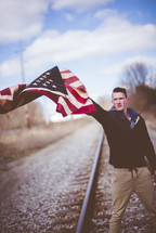 man holding an American flag standing on train tracks 