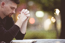 man praying over an opened Bible outdoors 