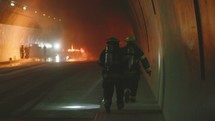 Firefighters inside a dark tunnel with emergency lights in the background