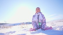 Happy child girl plays with a snow in winter day. Girl enjoys winter, frosty day. A young girl throws up snowflakes in the bright sun. Snowflakes fly at sun light. Slow motion.