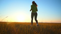 Athlete young beautiful slender woman in sports uniform running on field at sunset. Active person outdoors in summer. Sporty lifestyle. Fitness training in fresh air jogging. Summer warm weather.