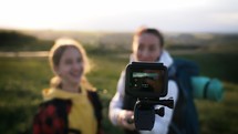 Young mother and teen daughter travelling through mountain recording travel vlog on action camera. Family of tourists walks at sunset. Adventure, healthy lifestyle. Tourists shooting self video.