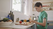 Young boy working in the kitchen slicing fruit for breakfast